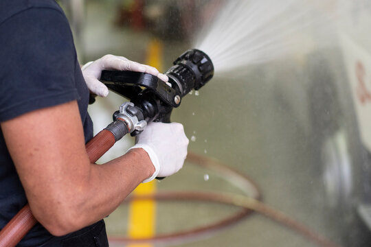 Side view of unrecognizable firefighter in latex gloves washing car with fire hose at station