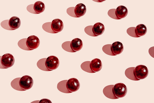 From above pattern of fresh red grapes arranged in lines on pink surface in studio