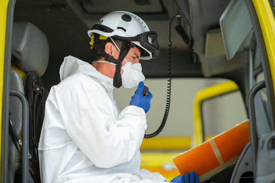 Side view of fireman wearing protective uniform and hard helmet with medical gloves sitting in fire engine speaking on walkie talkie