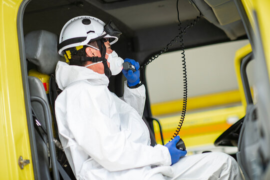 Side view firefighter wearing respirator and helmet sitting in fire car and using walkie talkie