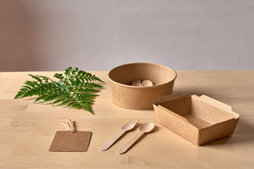 Recyclable carton food package and wooden fork and knife placed on table with fern leaf