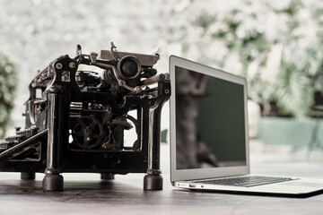 Modern netbook and old fashioned typewriter placed on wooden table on terrace