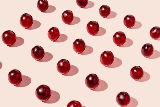 Top view of pattern of fresh red grapes arranged in lines forming a square shape on pink surface in studio