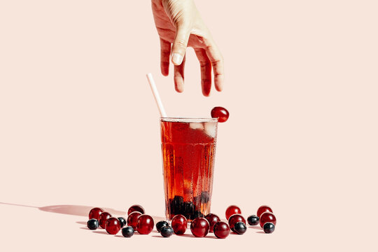 Anonymous person taking glass of tasty juice in glass placed on pink background with ripe grapes