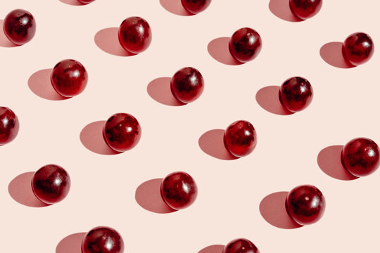 From above pattern of fresh red grapes arranged in lines on pink surface in studio