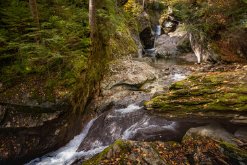 Rocky waterfalls passing shady forested area in sunlit fall colors