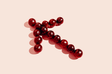 Top view of red grapes arranged in arrow showing direction on pink background