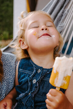 Content little kid eating homemade popsicle on stick while relaxing on terrace in summer