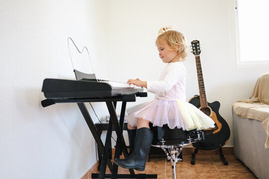 Side view of schoolgirl in fluffy skirt sitting at synthesizer and preparing for music class looking at camera