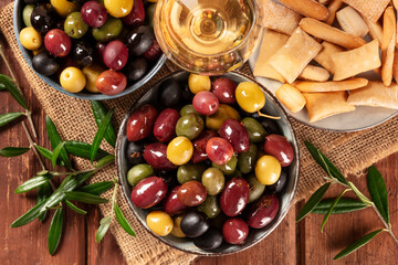 Olives. A variety of green, black and red olives, with wine and breadsticks on a rustic wooden background, overhead close-up shot