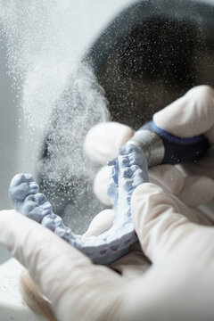 From above of crop anonymous dentist in medical gloves grinding dental prosthesis with professional tool while working in modern laboratory