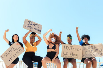 Group of multiethnic female activists protesting with raised arms in city with carton placards with black lives matter inscription and looking at camera