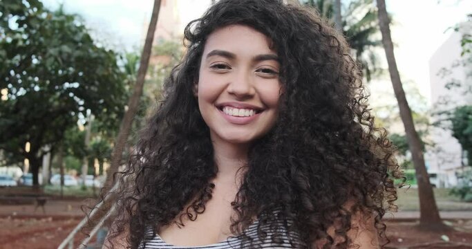 Young afro-american woman with curly hair looking at camera and smiling. Cute afro girl with curly hair smiling looking at camera. 4K.