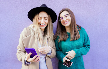 Portrait of two young friends using their mobile phone in violet background -  Lifestyle and...