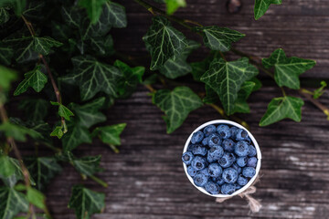 Some blueberries in a decorate small bucket on wooden banch in the garden on summer sunset