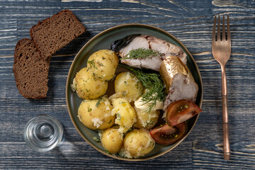 Hot smoked mackerel fish and young boiled potato on the plate with a glass of vodka and black bread, top view, closeup