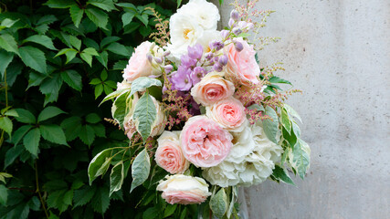 An elegant bouquet of delicate roses. A romantic photo of a bouquet of flowers against a background of a concrete wall with space for text. Still life of flowers and greenery in the French style.