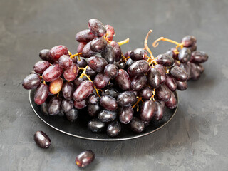 Black grapes on a black plate on a black background.