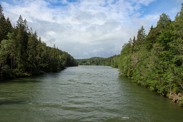 View of the Gota river in western Sweden with dense forest on both sides and a blue sunny sky, partly cloudy