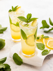 Lemon lemonade with ice and mint on a white plate on a white-gray background.