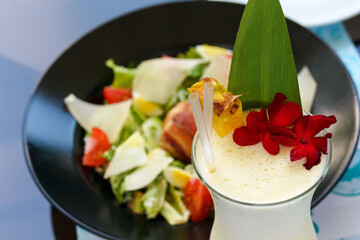 Sweet Caribbean cocktail Pina Colada of rum, pineapple juice and coconut liqueur in a glass glass. Close-up. Alcoholic tropical drink, decorated with flowers and a slice of pineapple. Romantic dinner.