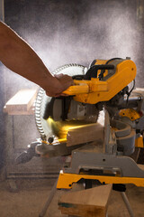 Carpenter working with power circular miter to cut wooden board against darkness.