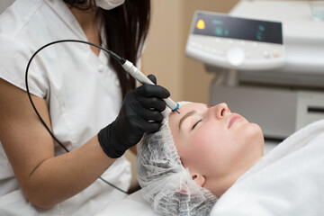 Therapist beautician makes a laser treatment to young woman's face at beauty SPA clinic. Close-up process of laser removal of blood vessels from the skin