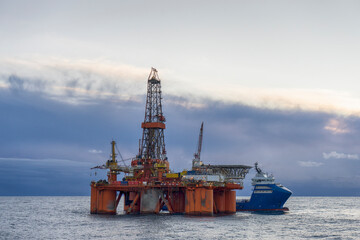 Offshore Jack Up Rig And Supply Ship In The Middle of The Sea at Sunset Time