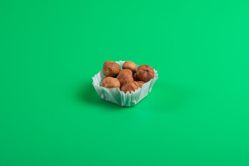 A serving of hazelnuts in a paper muffin cup on a green background.