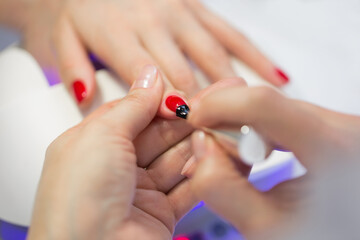 Naklejka premium Manicurist master makes red manicure on young woman hand. Woman nail master doing nails to a girl client at a beauty salon. Care for hands