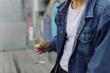 Young man in blue jacket holding glass of white wine on terrace. Copy space, summertime relax concept.
