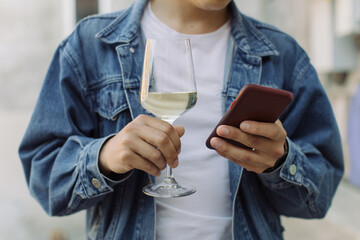 Man in blue jacket holding glass of wine and text messaging on smart phone. Summertime relax concept.