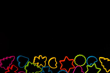 multi-colored plastic molds of various shapes grouped below for making cookies on a black background. Culinary concept. Flat lay with copyspace.