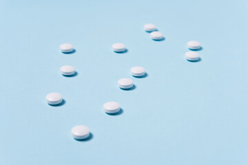 Photo on a medical topic. White tablets are randomly scattered on the blue table.