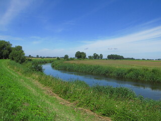 Rural landscape on the outskirts of Braniewo town in northeastern Poland, in the Warmian-Masurian Voivodeship, On the trail of Pomeranian Way of St. James - green fields, Pasleka river, blue sky
