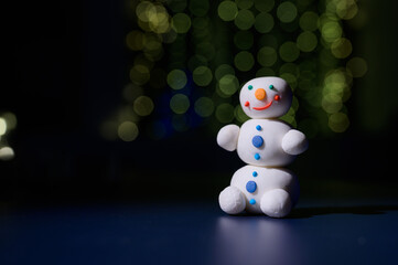 Cute snowman and little Christmas trees made of marshmallows on the background of Christmas lights. White mug of hot chocolate and sweets.