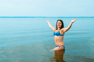 A brunette woman in a blue swimsuit at sunrise in the azure water near the shore.