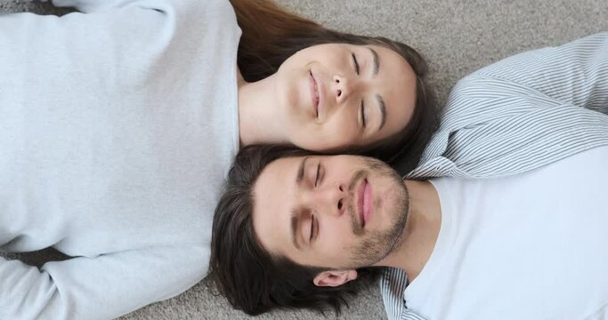 Carefree couple lying on carpet with eyes closed at home