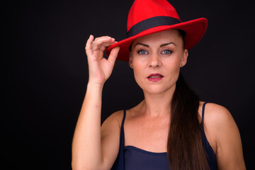 Mature beautiful woman wearing red fedora hat against black background