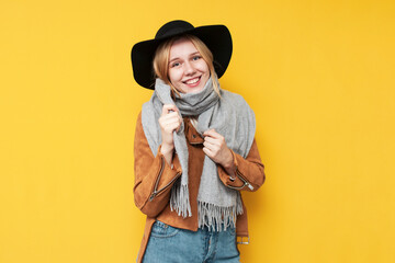 Fototapeta na wymiar girl in autumn clothes and a scarf smiles on a yellow isolated background, a woman warmly dressed in autumn