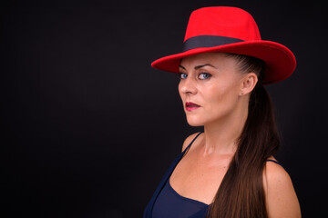 Mature beautiful woman wearing red fedora hat against black background