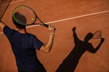 shadow of a tennis player on an outdoor clay tennis court performing a serve