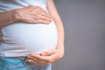 Pregnant woman holds hands on belly on a gray background. Copy space, pregnancy, motherhood, people and expectation concept. Close-up, copy space, indoors. Toned photo of pregnancy.