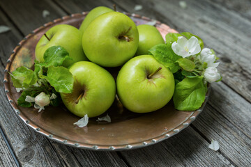 Green apples with apple tree flowers in an old copper dish on a wooden table