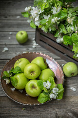 Green apples with apple tree flowers in an old copper dish on a wooden table