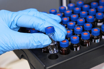 Close up woman hand in a rubber gloves put sample in a glass vial with blue cap into the...