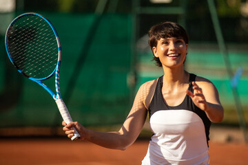 a smiling woman playing tennis outdoors on a clay court