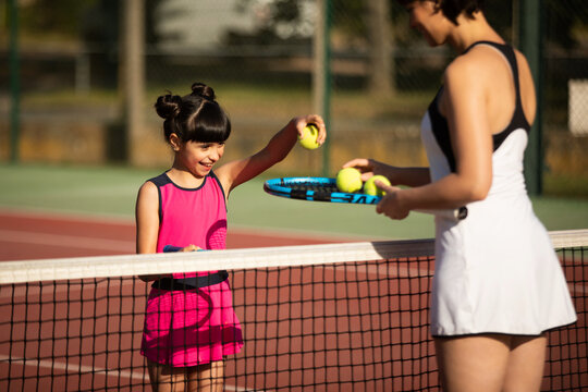 a mother and daughter playing tennis together outdoors on a clay court
