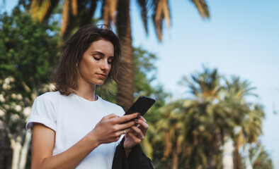 pretty woman writes message on mobile smartphone while walking Park barcelona on a warm summer day, hipser girl listens to music on earphones and searches for information using cell phone