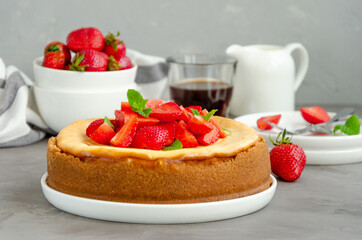 Homemade cheesecake New York with fresh strawberries on a white plate with coffee on a gray stone background. American cuisine.